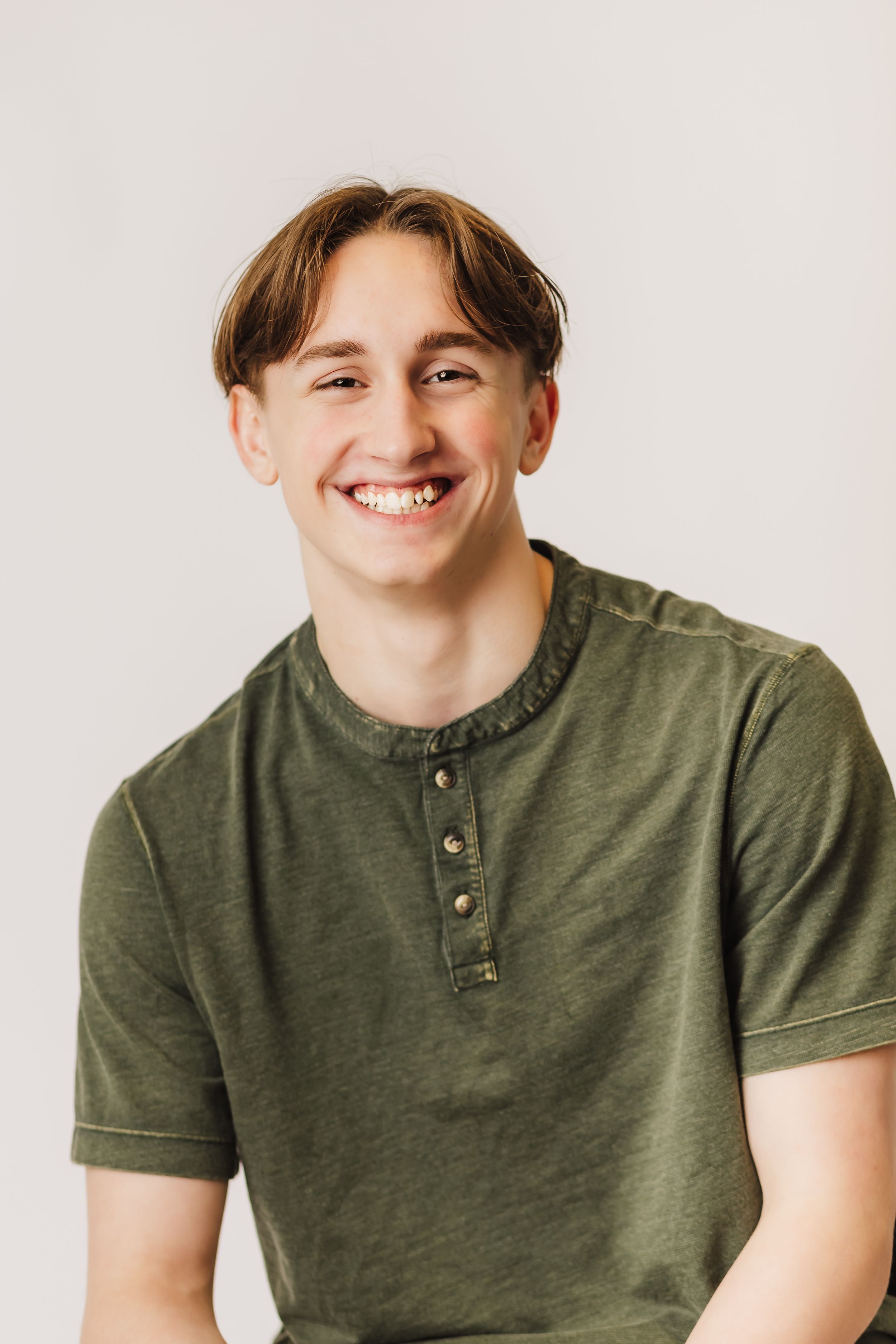Casual portrait of young man in olive henley shirt smiling against white background.