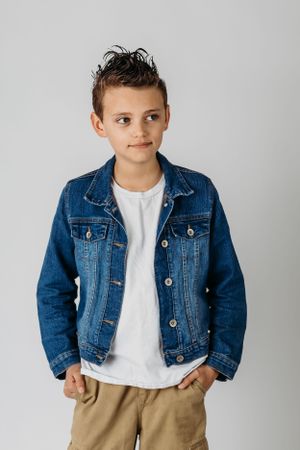 Child in denim jacket and white t-shirt poses against grey background.