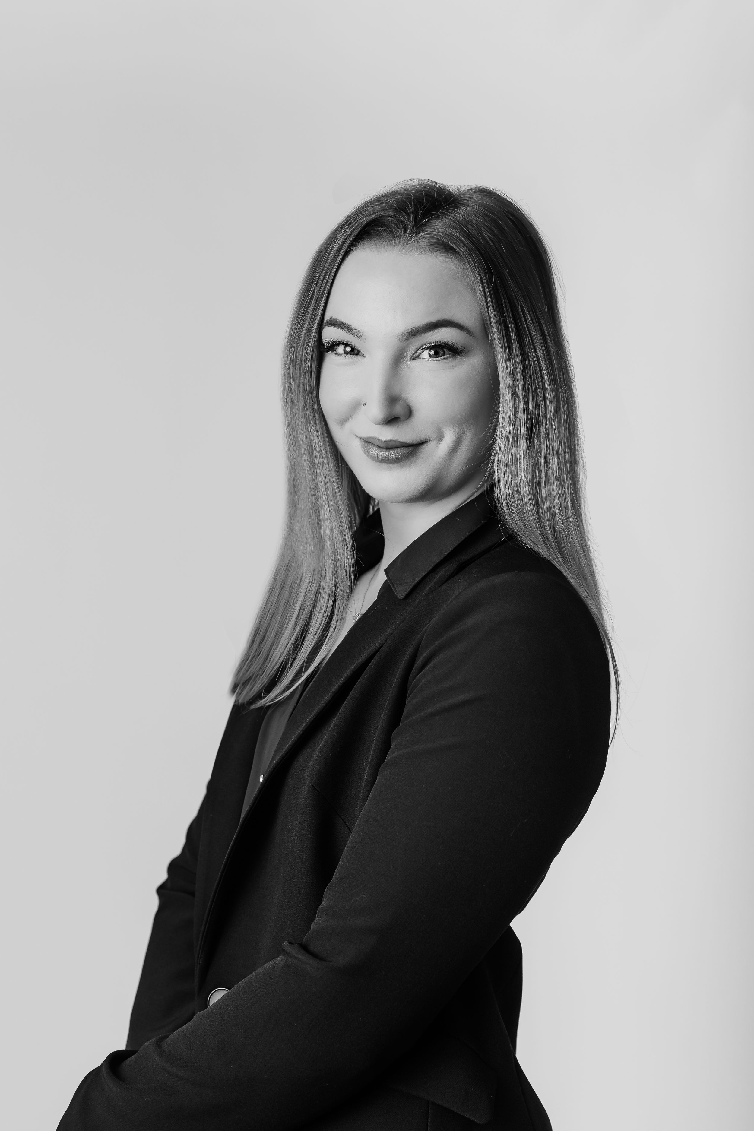 Professional headshot of woman in black blazer smiling confidently against light background.
