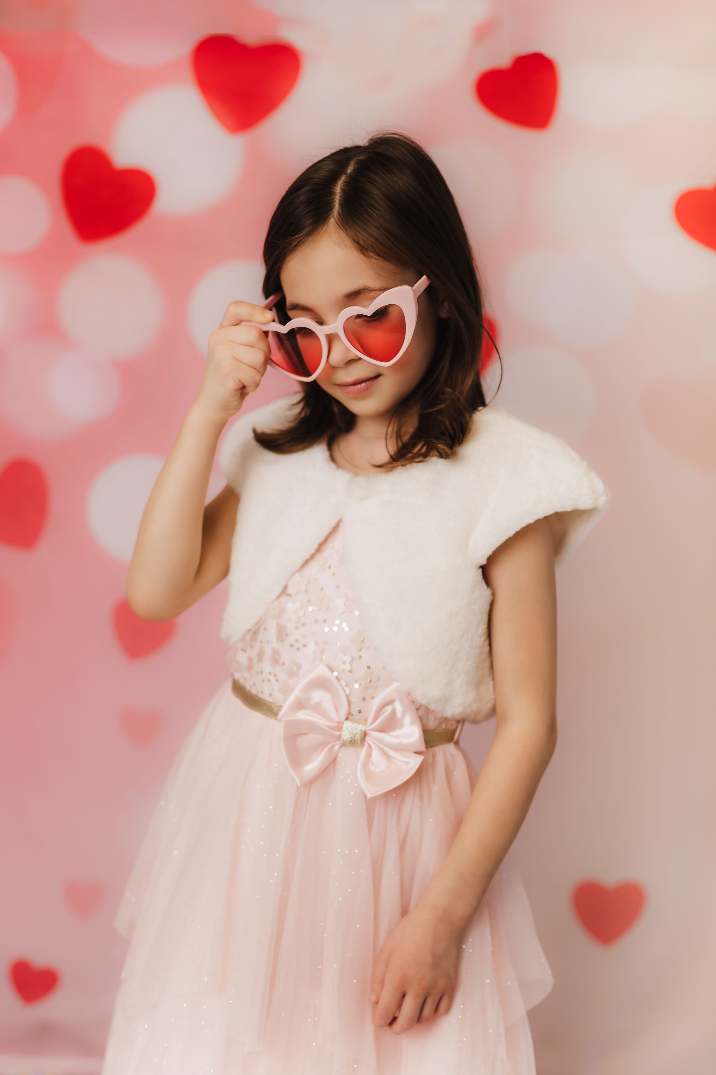 Person wearing heart-shaped sunglasses and pink tulle dress poses against red heart backdrop.