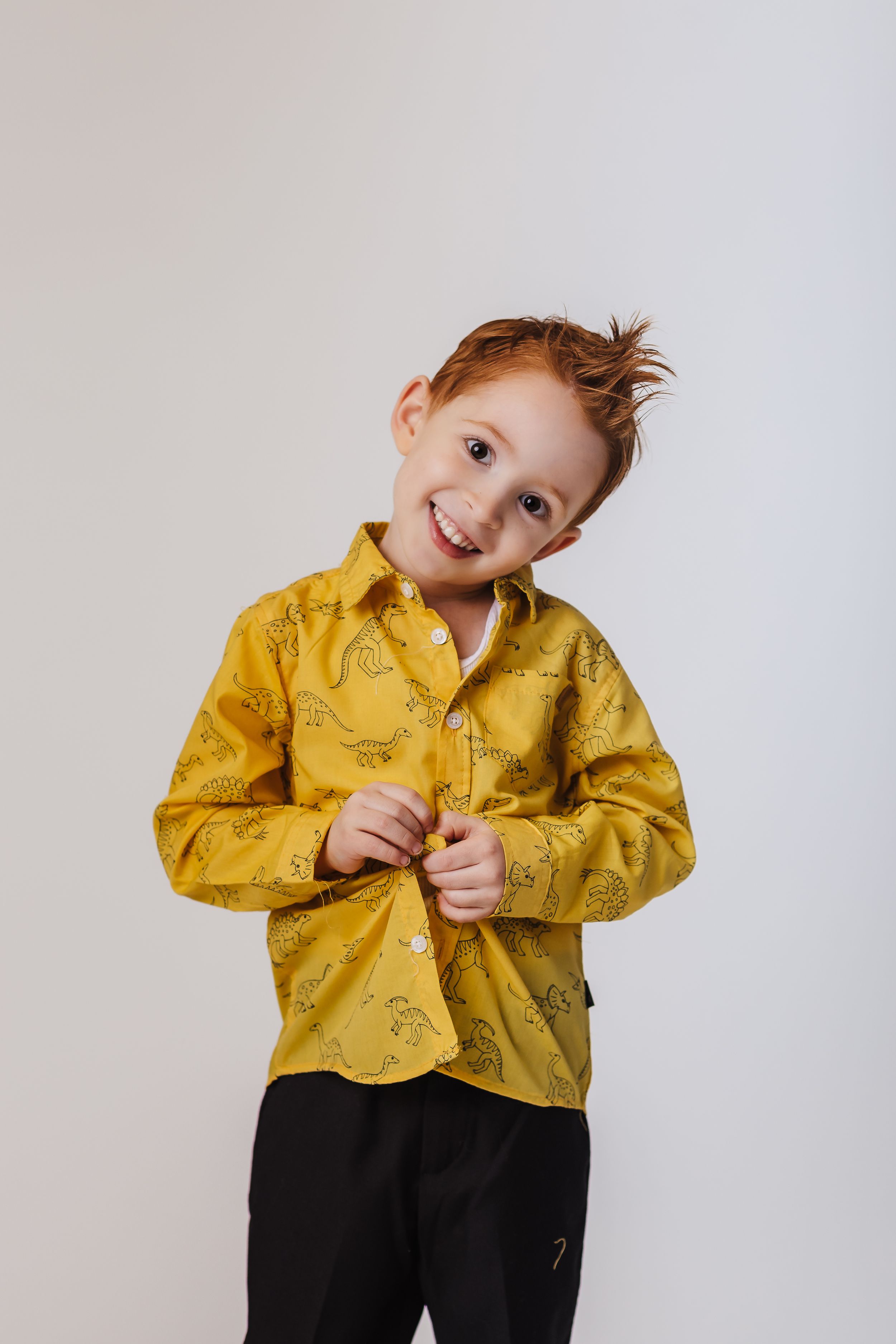 Person in yellow patterned button-up shirt poses playfully against white background.