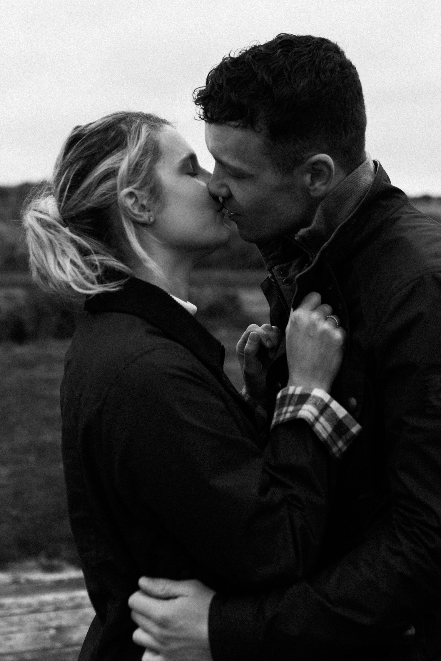 Intimate black and white portrait of a couple sharing a romantic kiss outdoors.