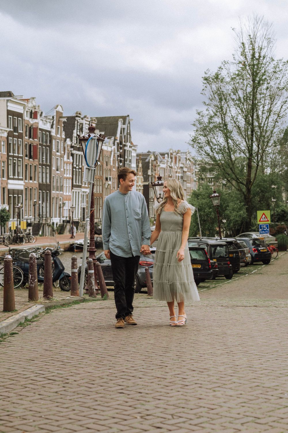 Two people stroll together along a scenic canal path with historic Dutch buildings in the background.