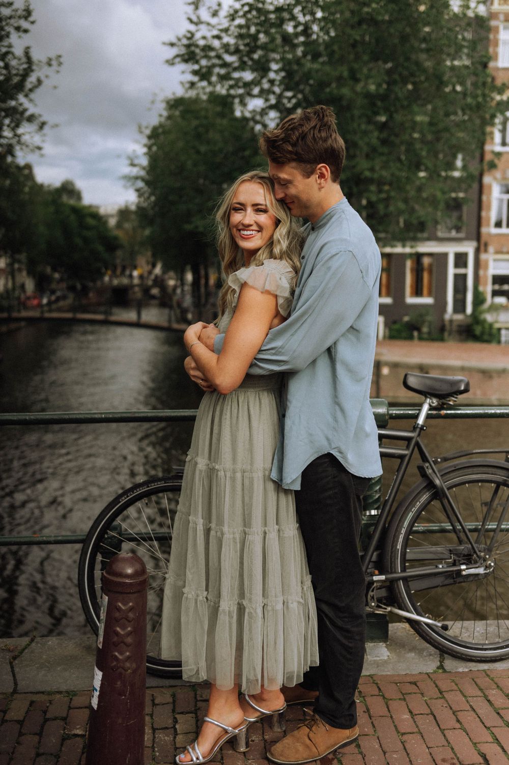 Couple embracing by a canal in Amsterdam with bicycles nearby.