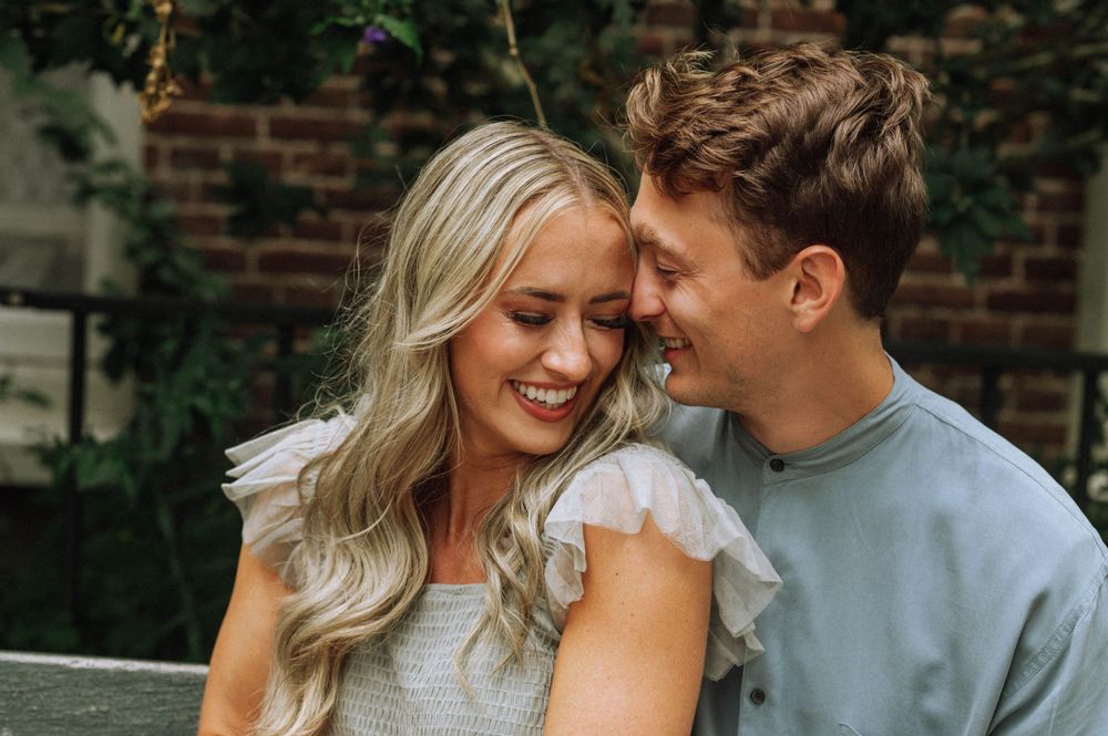A couple shares a playful moment while sitting on a bench surrounded by greenery.