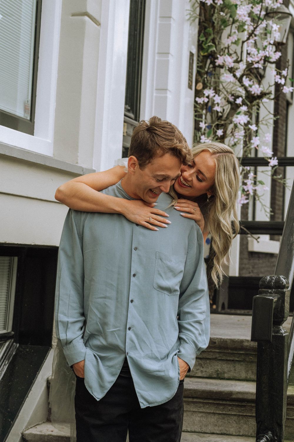 A couple embraces tenderly against a white building with climbing vines.