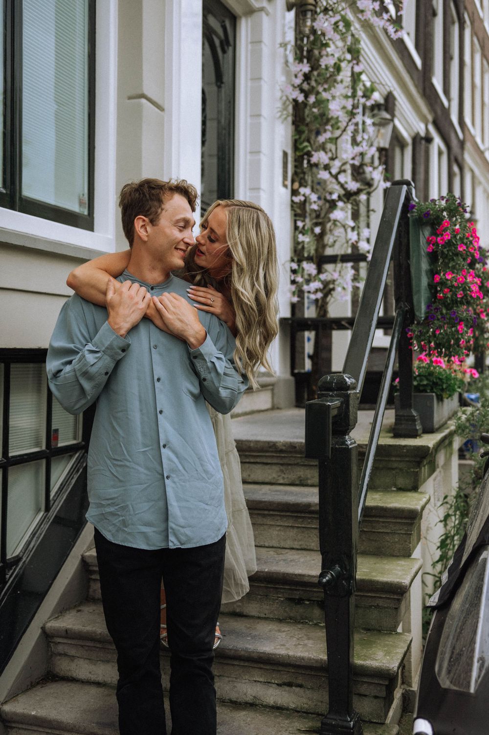 Intimate couple moment captured on white stone steps with flowering plants and classic architecture.