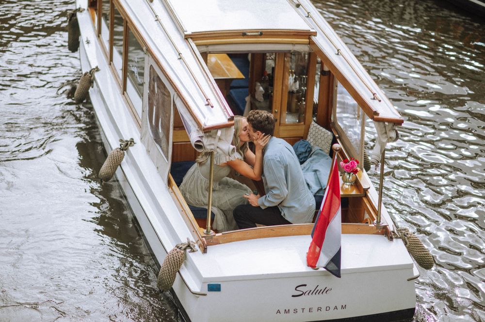 Wooden tour boat named Amsterdam navigates through narrow canal waters.