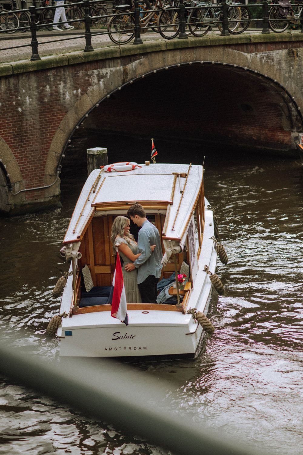White canal boat passes under brick bridge arch in Amsterdam's historic district.