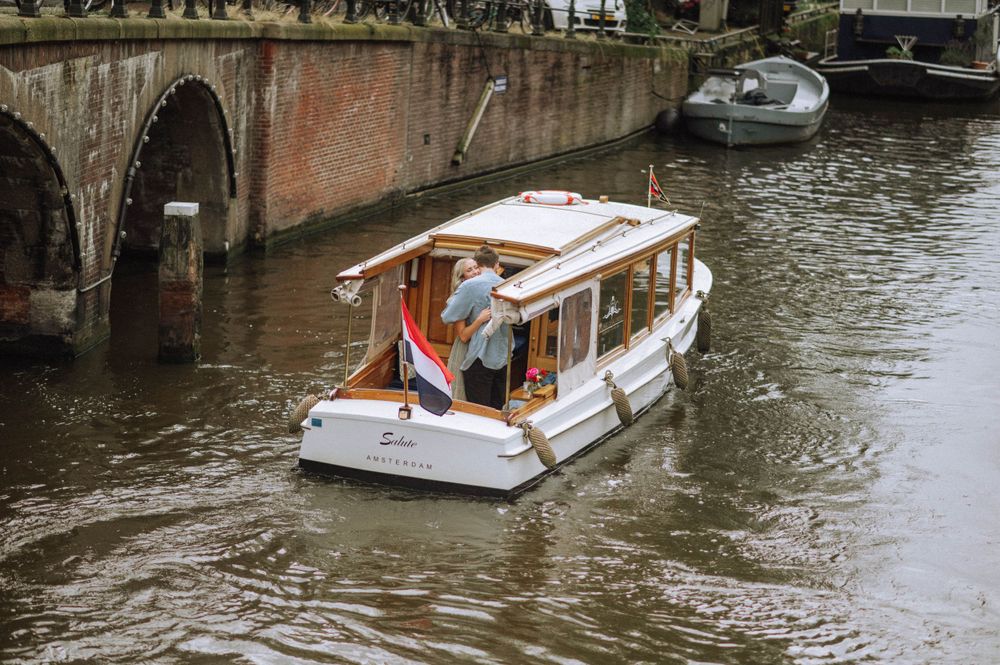 Multiple tour boats navigate Amsterdam's picturesque canal system on a cloudy day.