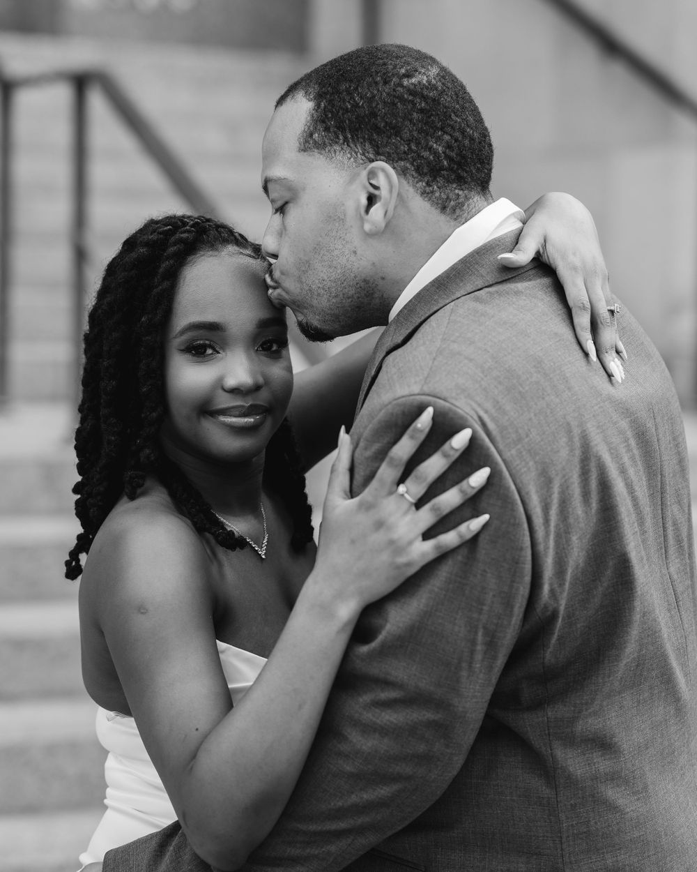 A romantic black and white portrait shows a couple embracing tenderly on stone steps.