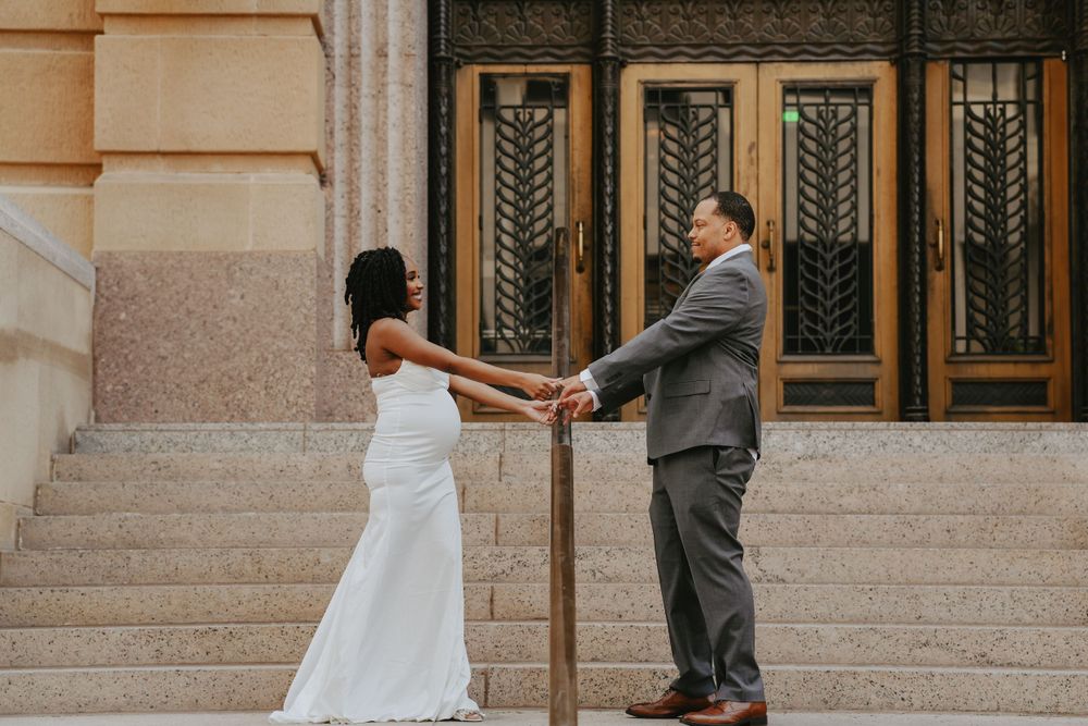 Couple in wedding attire hold hands while standing on stone steps in front of ornate vintage doors.