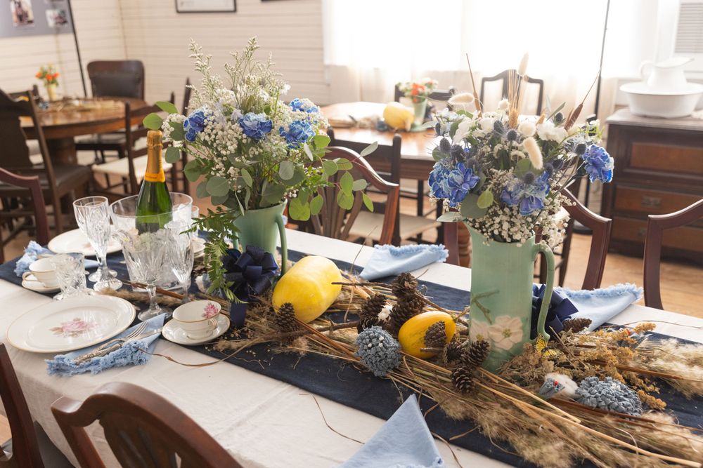 A table centerpiece with blue hydrangeas and white flowers in vases alongside citrus fruits and driftwood decorations.