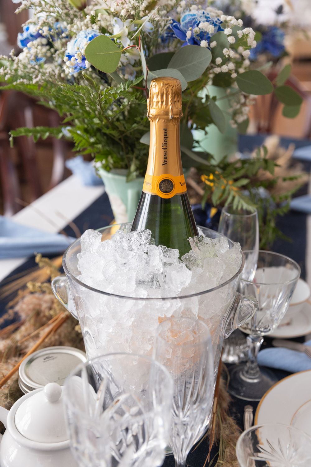 A champagne bottle chilling in an ice bucket with crystal glasses and floral arrangements on an elegant table setting.