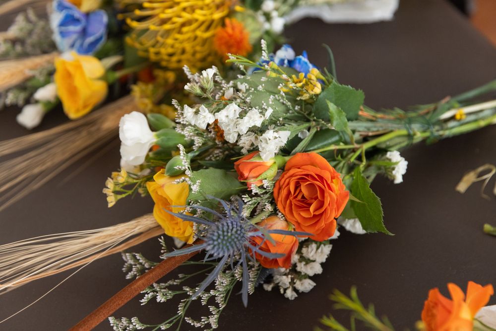 A rustic wedding bouquet with orange roses, yellow flowers, wheat stalks and white baby's breath on dark wood surface.