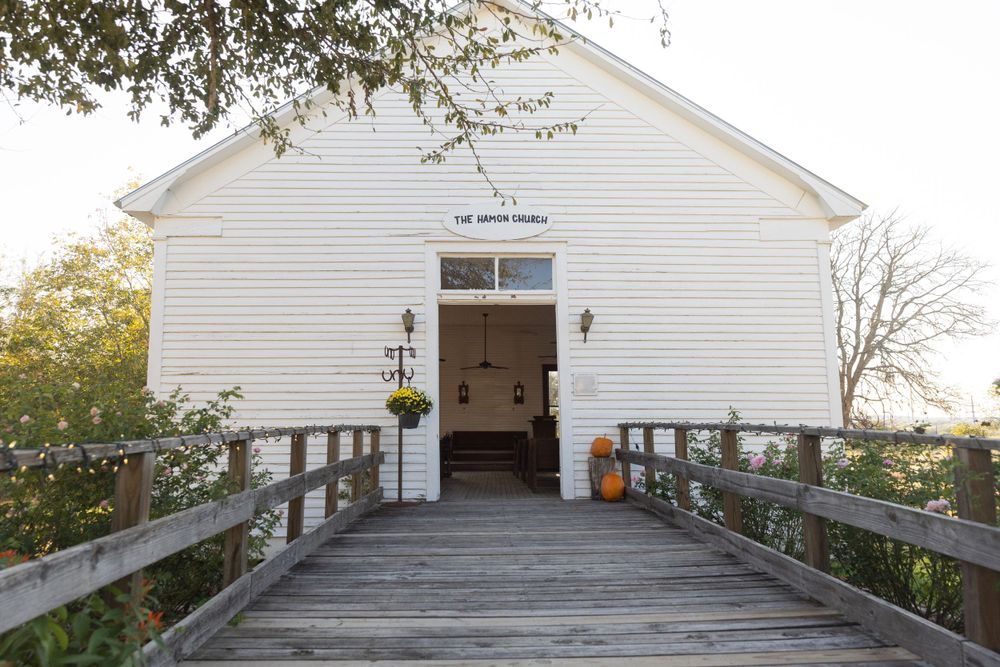 White wooden chapel with a wooden boardwalk entrance decorated with fall pumpkins and wreaths.