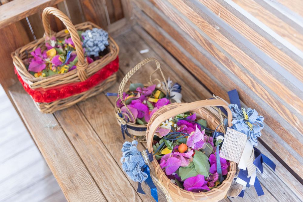 Two woven baskets filled with purple and blue flowers sit on a wooden deck.