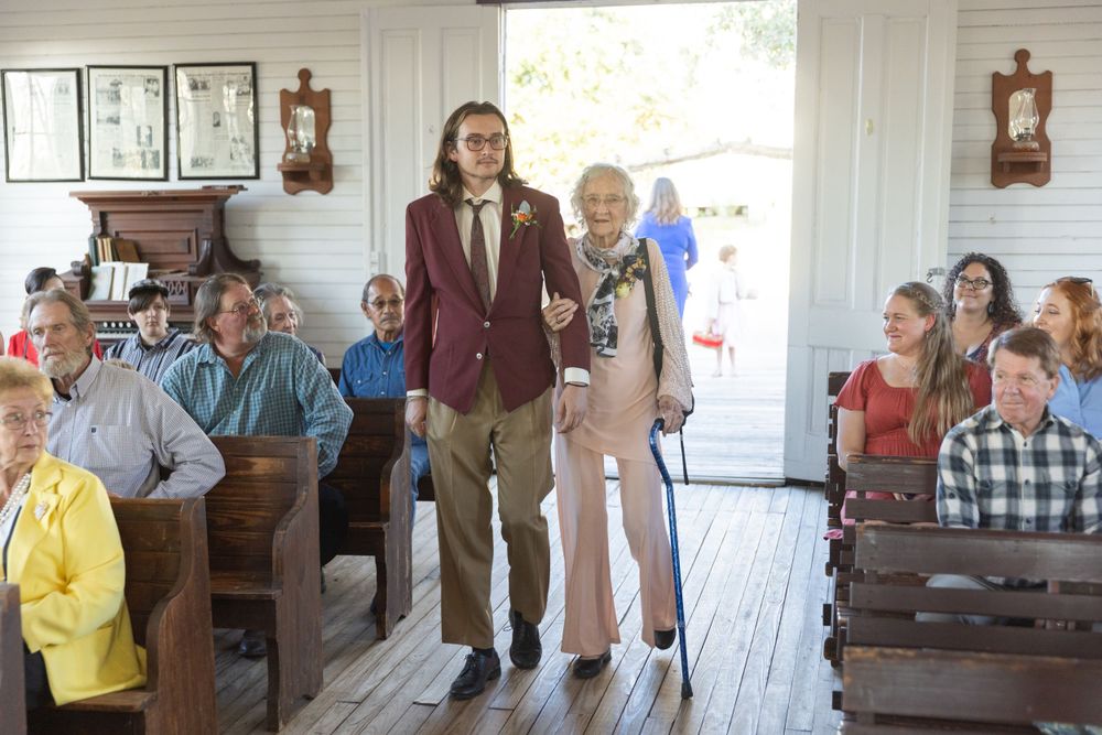 Wedding ceremony in a rustic white chapel with wooden pews filled with guests.