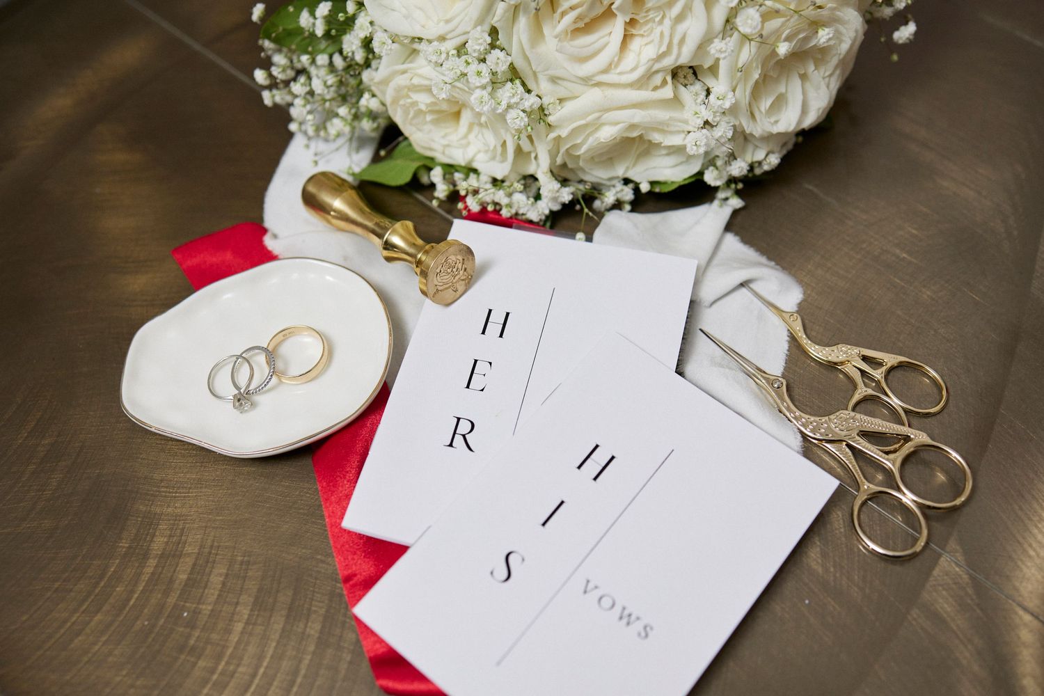 Wedding details featuring white roses and invitation cards with gold rings.