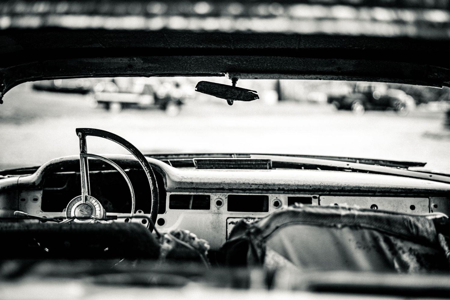 Black and white interior view of vintage car dashboard through windshield.