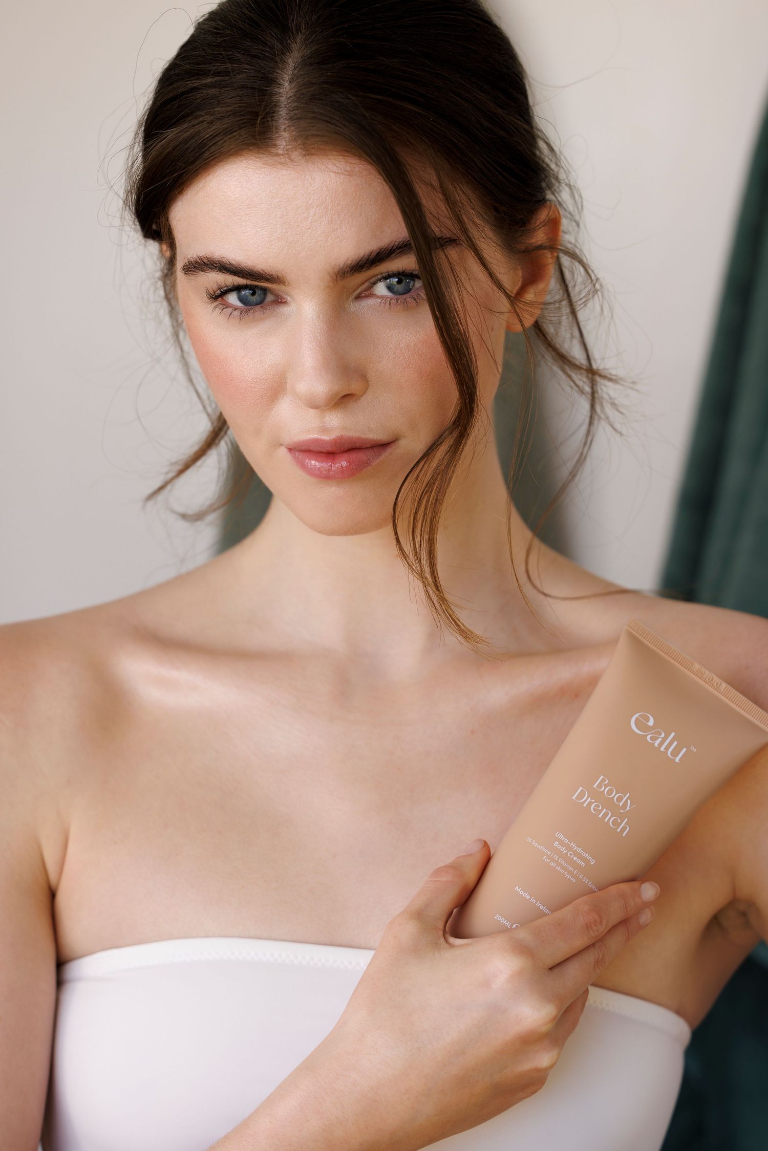 Beauty product advertisement featuring model holding cream tube in white strapless top.