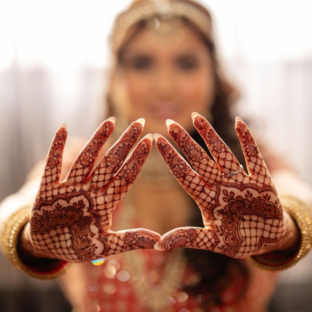 Bride displaying intricate red henna mehndi designs on both hands at an Indian wedding ceremony.