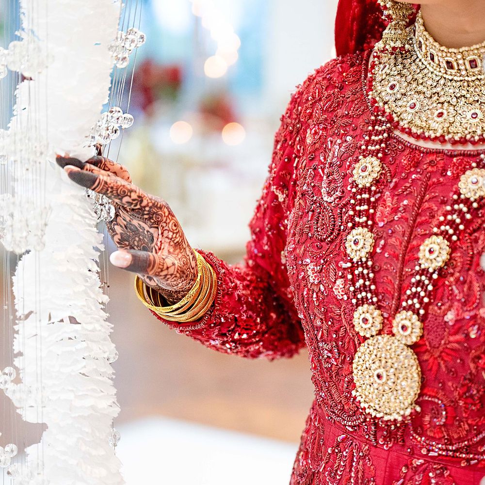 Detail shot of Indian bride in red embroidered lehenga with gold jewelry and henna hands.