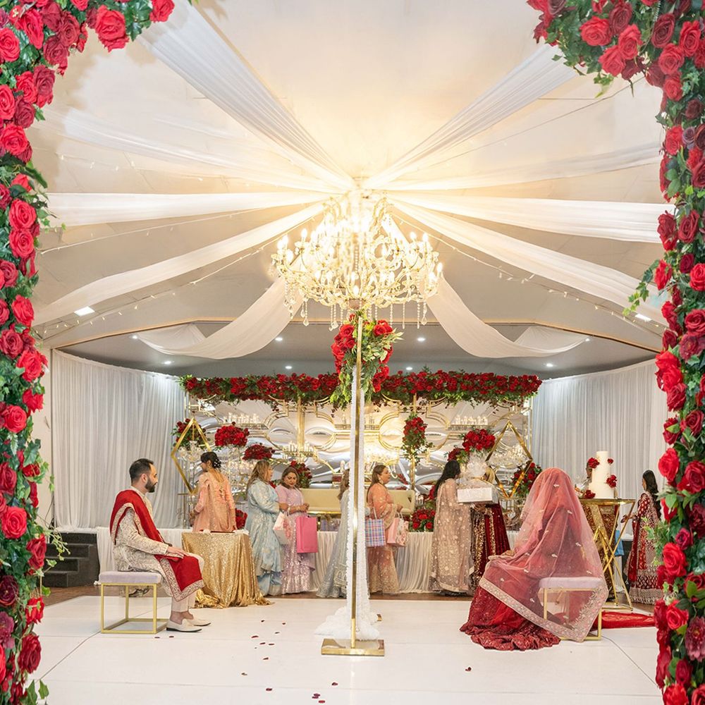 Elegant South Asian wedding ceremony under a chandelier-lit tent adorned with red roses and white draping.