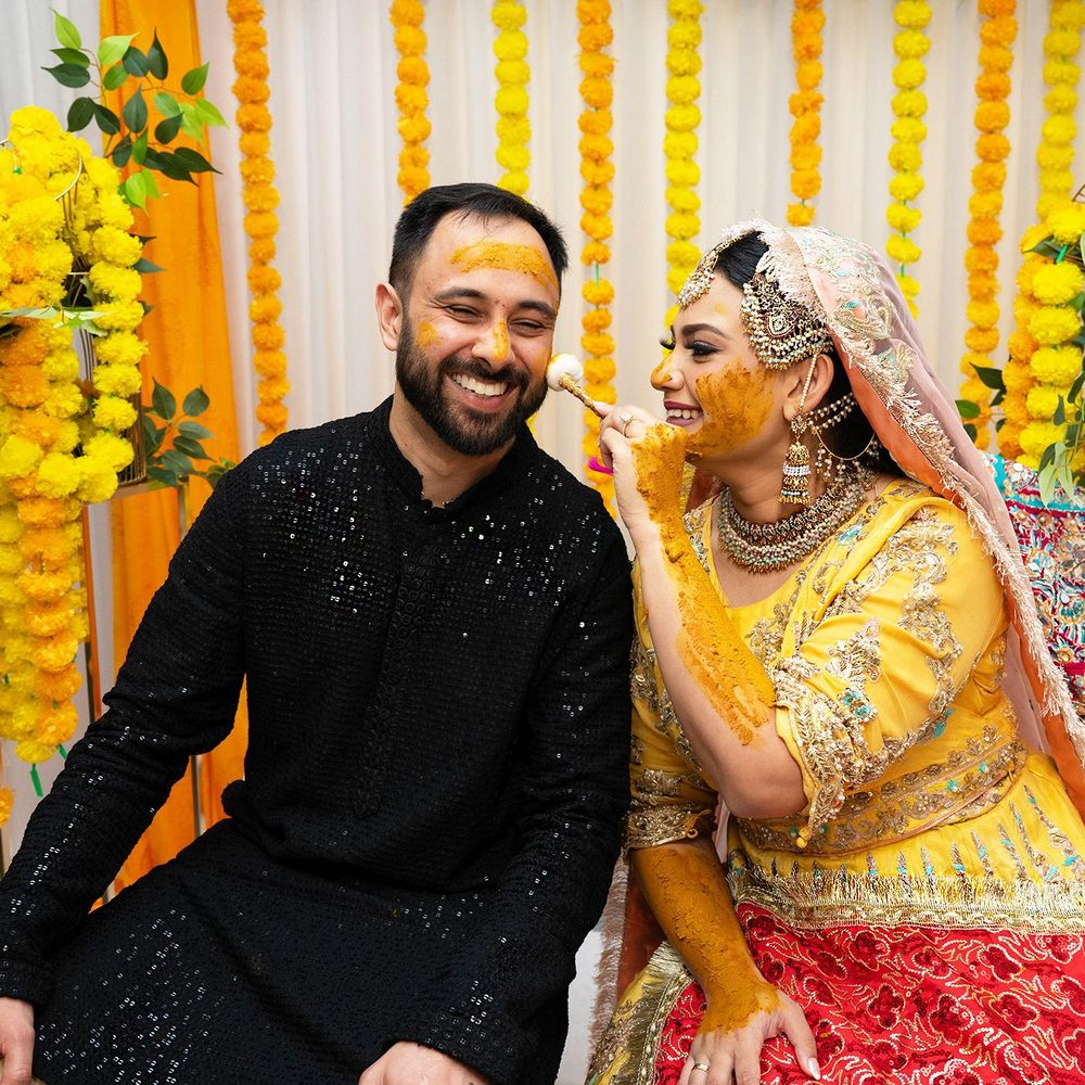 Couple laughing joyfully during a vibrant Haldi ceremony with yellow floral backdrop.