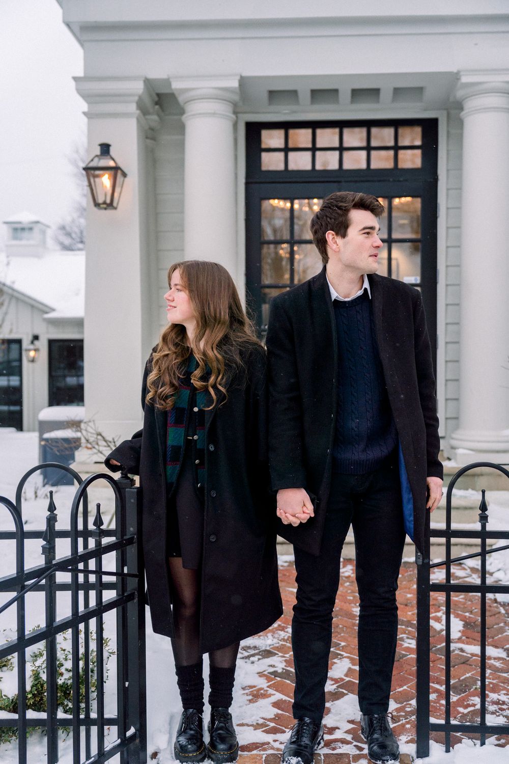 Couple holding hands outside white colonial building with black iron fence.