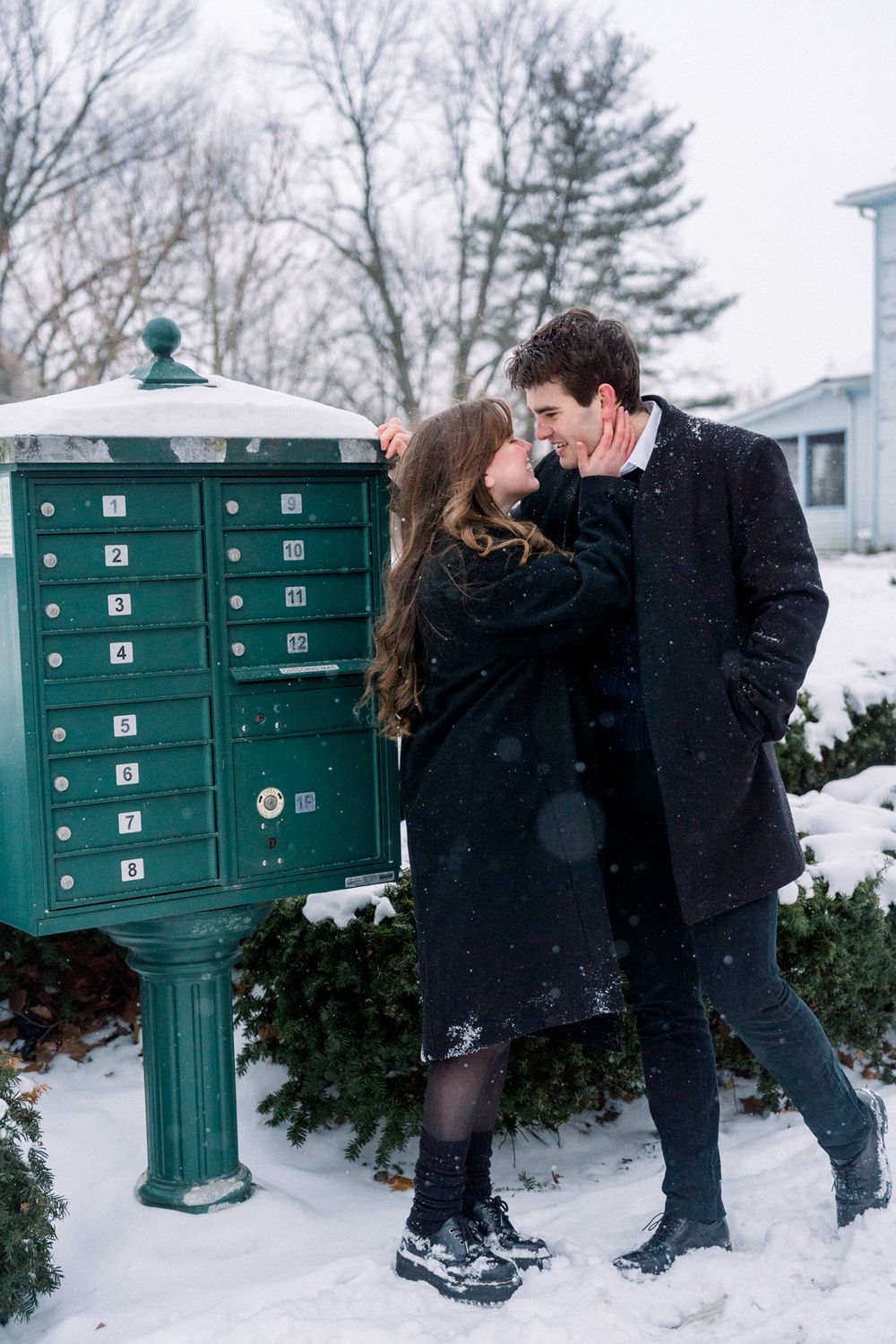 A couple shares a tender moment by a green community mailbox in the snow.