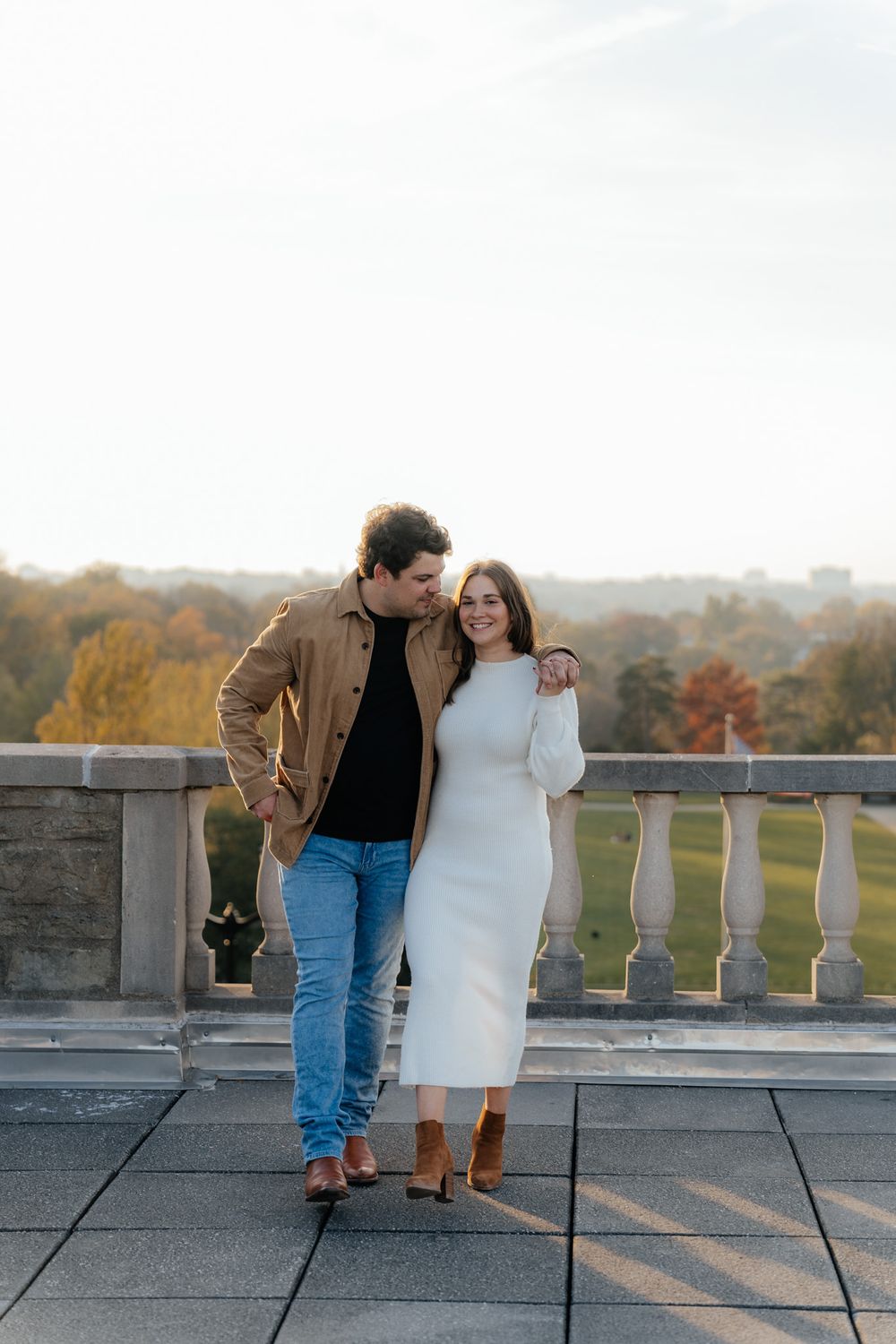 Couple walking together on stone terrace with fall foliage in distance.