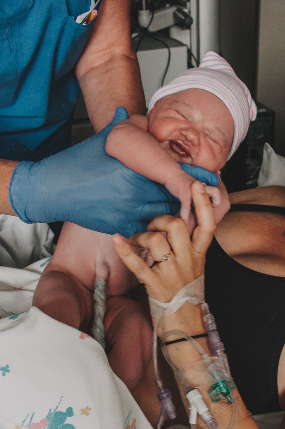 Newborn baby being held by gloved medical professional moments after birth in hospital delivery room.