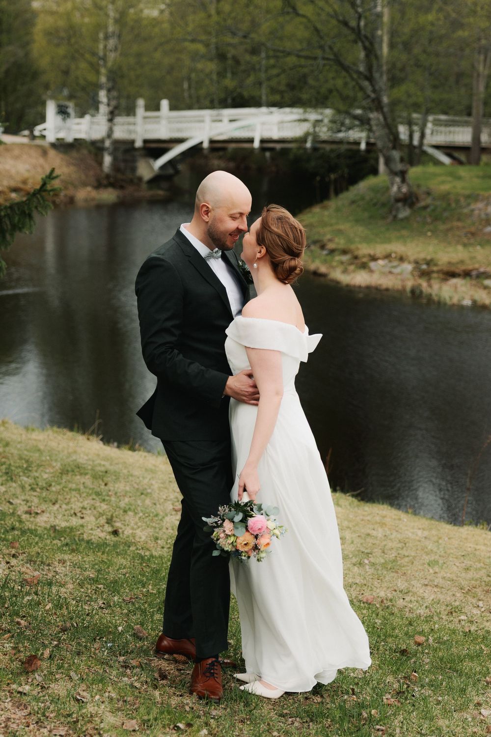 Newlywed couple shares intimate moments by a serene lake during their outdoor wedding photoshoot.