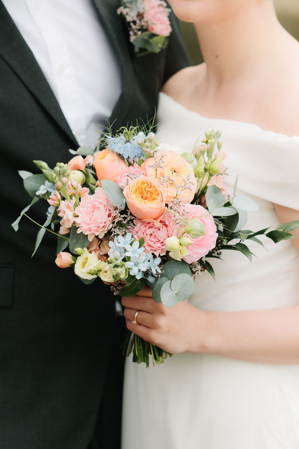 Elegant bridal bouquet features peach and pink roses with delicate eucalyptus leaves against formal attire.
