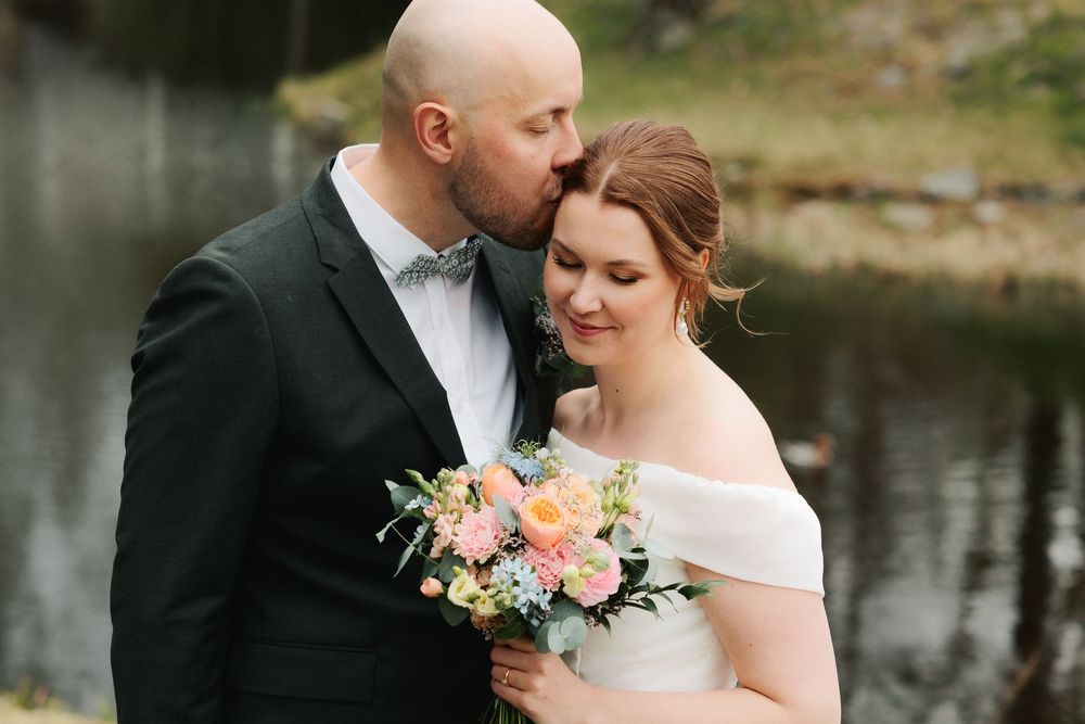 A couple shares an intimate moment during their wedding photoshoot by a serene waterfront setting.