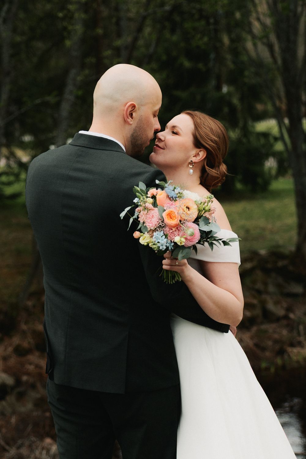 A romantic wedding couple shares intimate moments in an outdoor garden setting with colorful floral bouquet details.