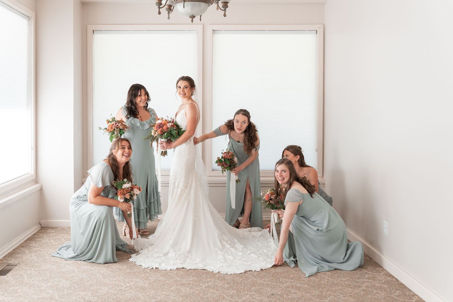 A bridal party poses together in a bright white room wearing soft blue bridesmaid dresses.