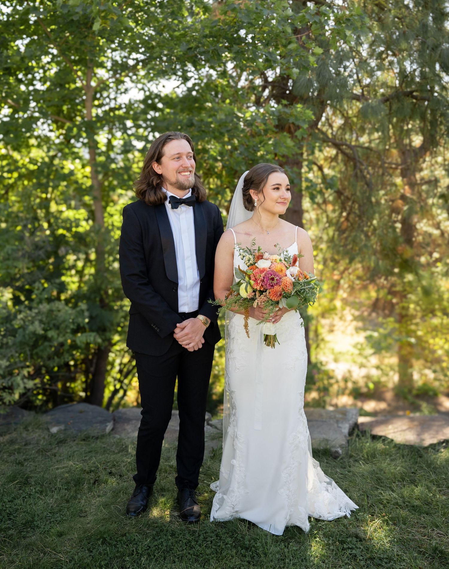 A wedding couple poses together in a garden with golden sunlight filtering through the trees.