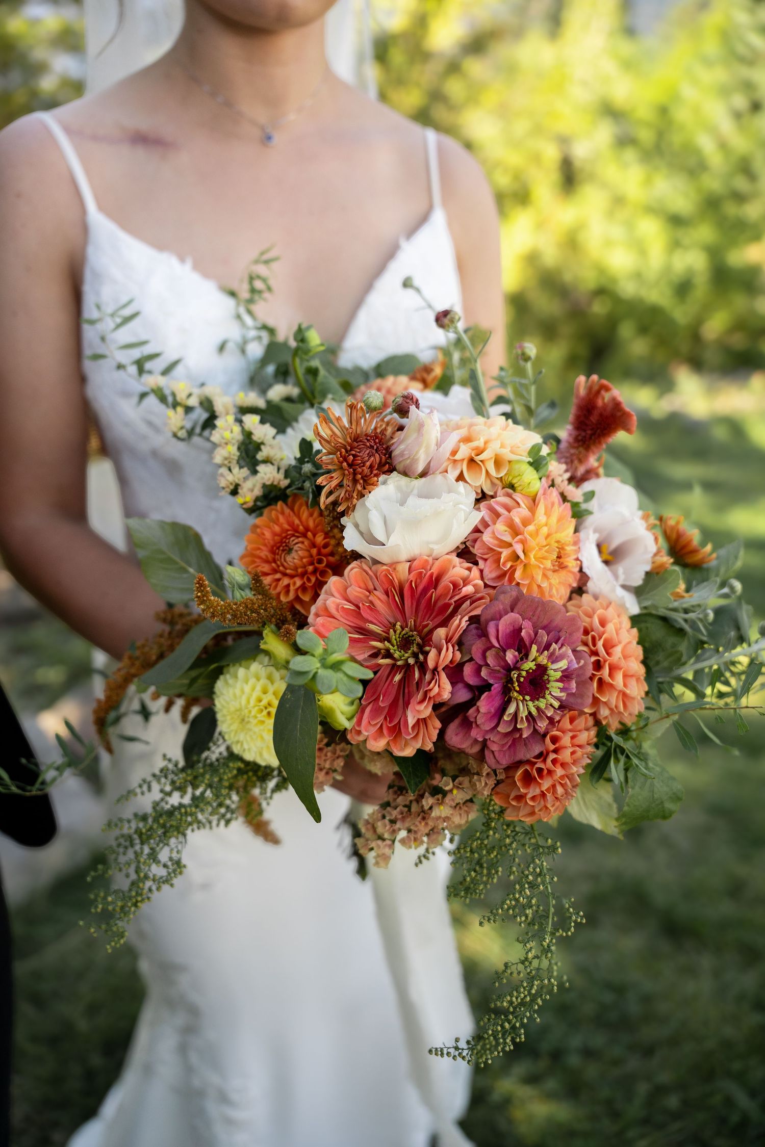 A vibrant fall-colored wedding bouquet with orange dahlias, roses, and cascading greenery.