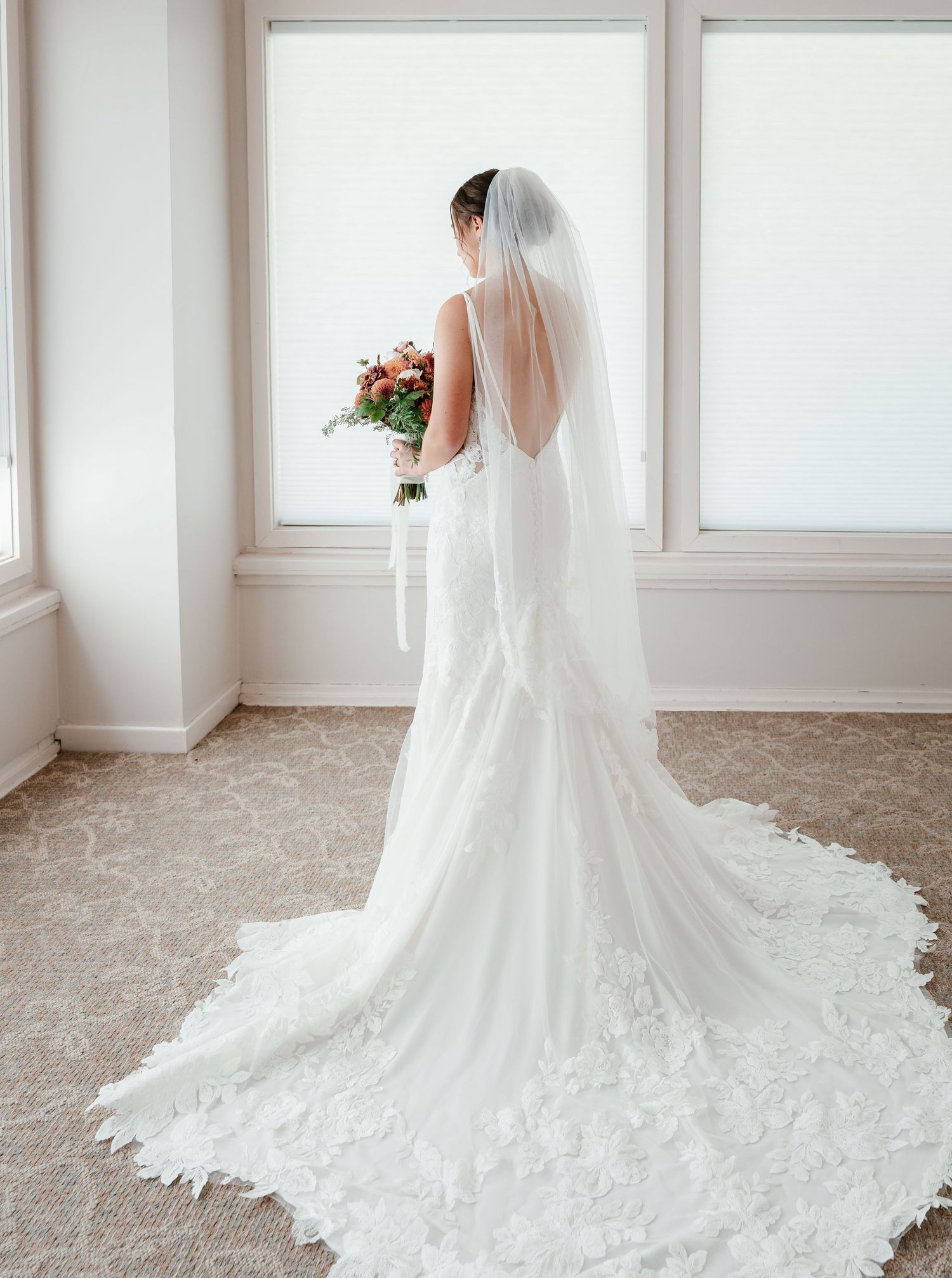 An elegant wedding dress with a dramatic train and open back silhouette photographed in a bright room.