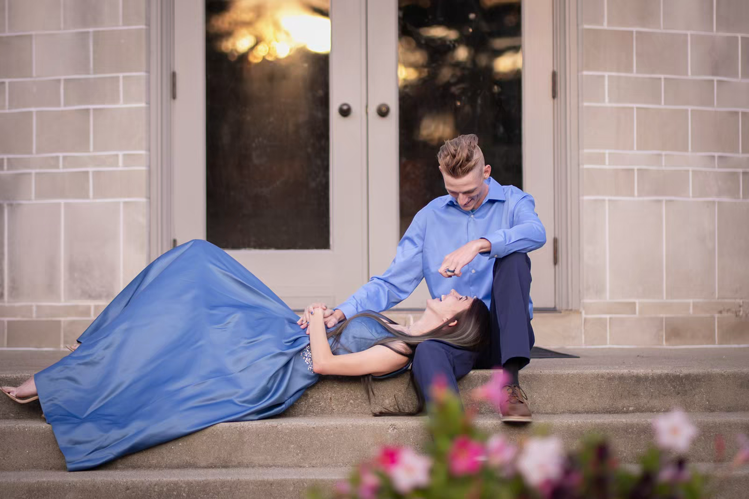 A couple shares a tender moment on stone steps outside a building.