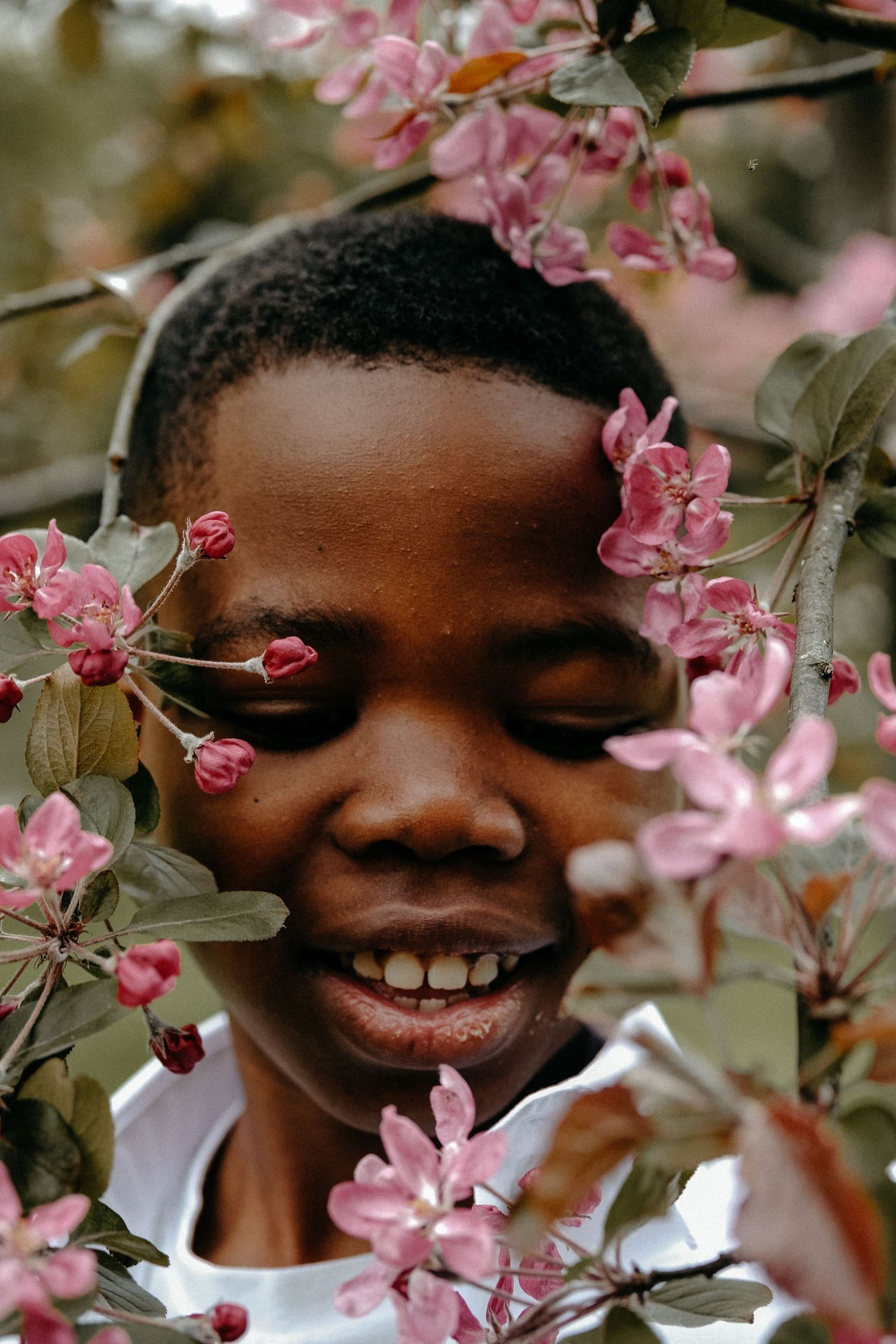 Outdoor portrait of a smiling child surrounded by spring blossom flowers during a lifestyle family photography session in Nunsmoor Park