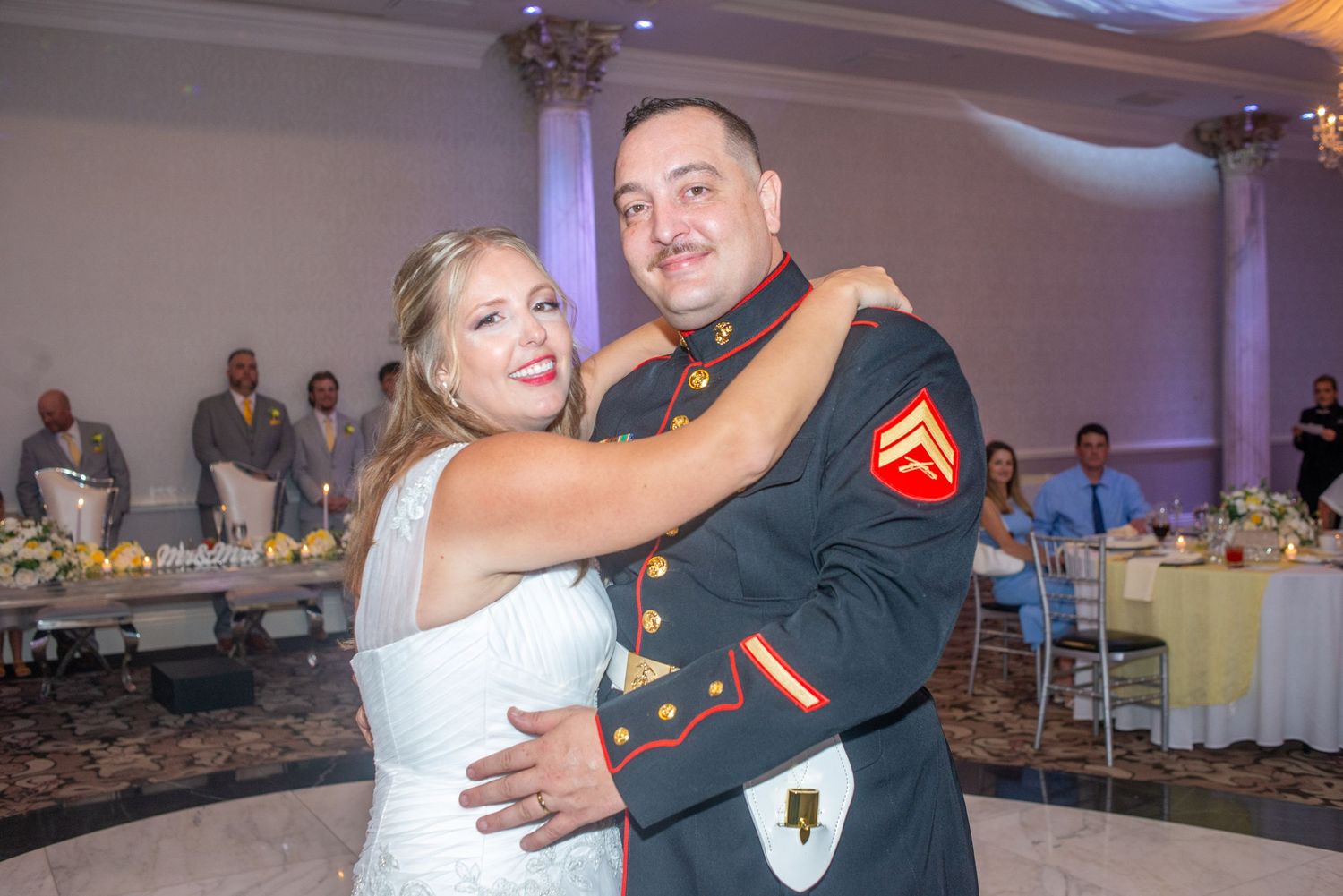 Couple dancing together at wedding reception in elegant ballroom with colorful ambient lighting.