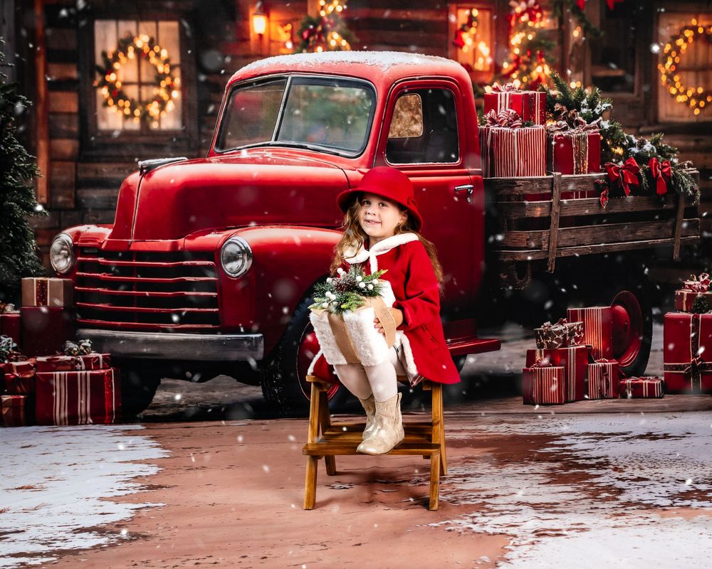 A vintage red pickup truck decorated for Christmas with wrapped presents and holiday lights in a snowy setting.
