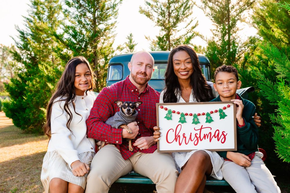 Family wearing coordinated red and white outfits poses together outdoors for holiday photos at sunset.
