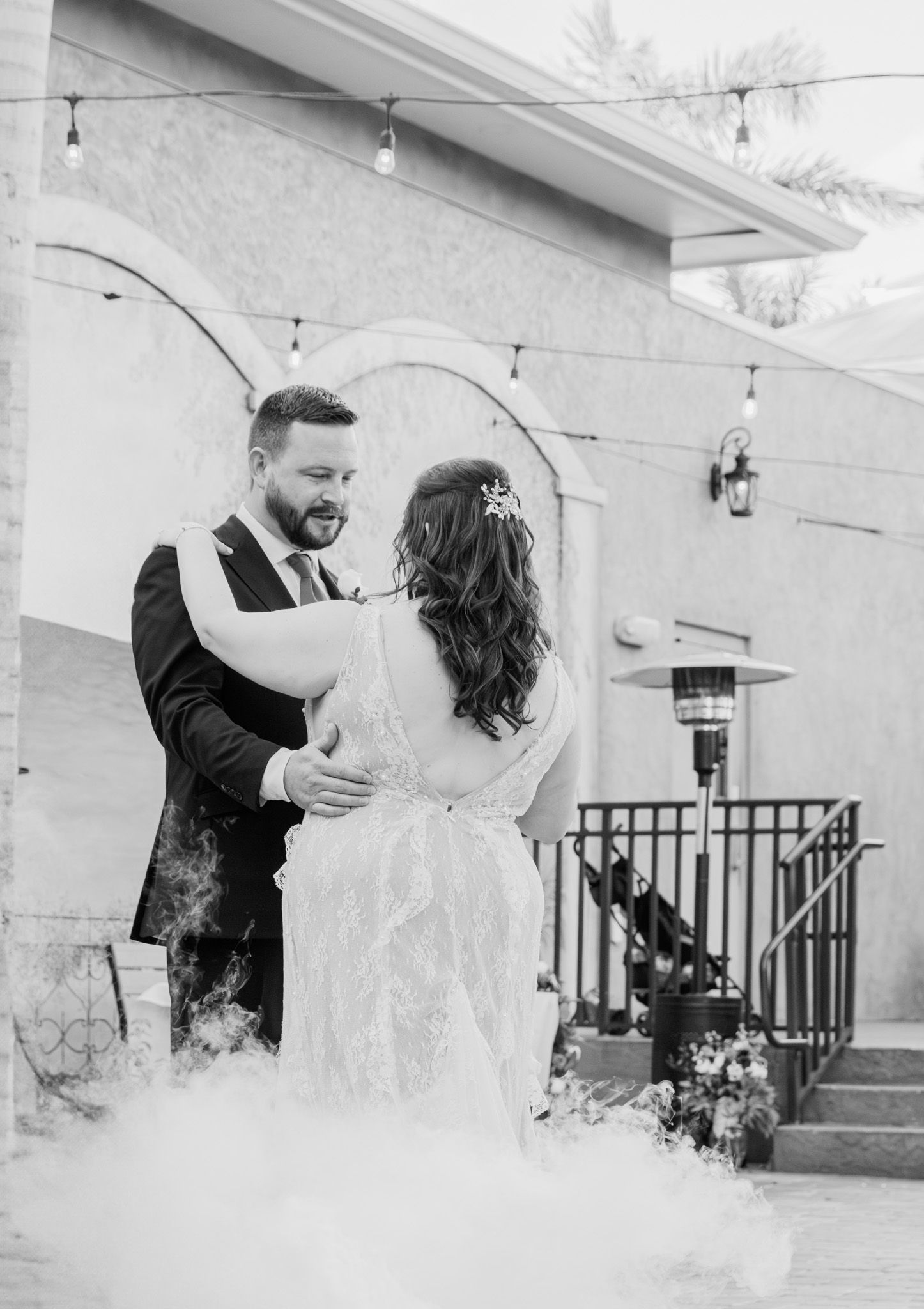Black and white photo of a bride and groom sharing their first dance surrounded by romantic fog at an outdoor wedding venue.