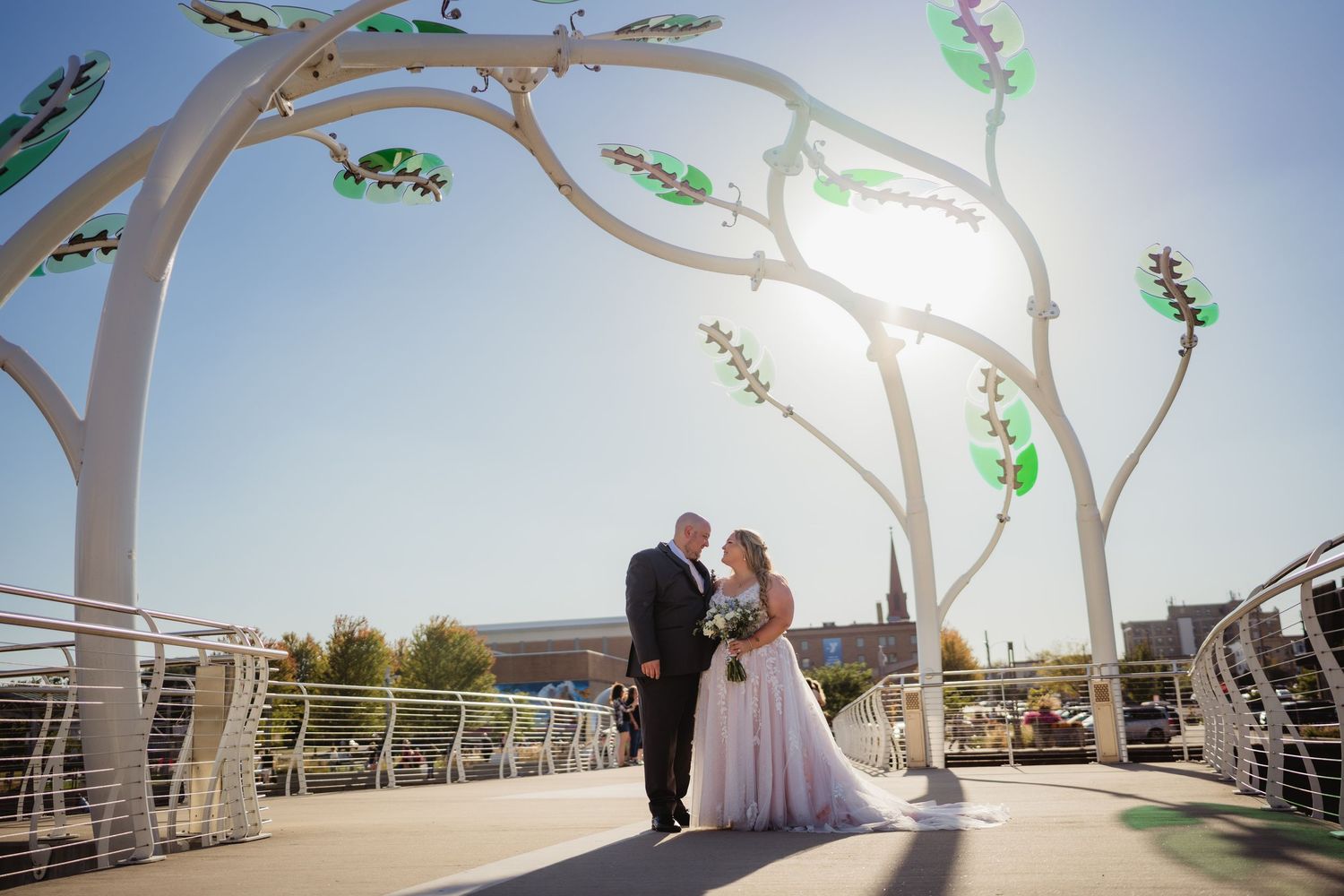 A couple shares a romantic moment under white architectural arches at an outdoor wedding venue.