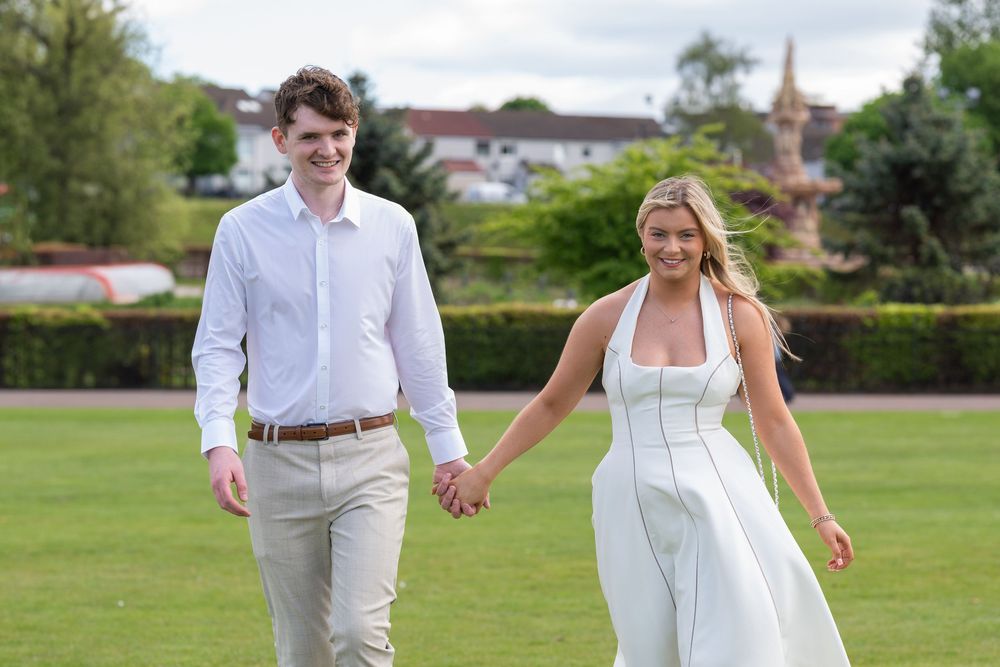 Couple walking hand in hand through sunny garden landscape.