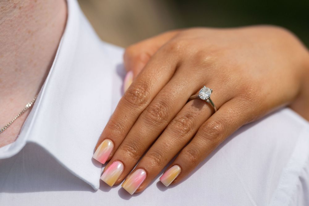 Close-up of a hand wearing an elegant solitaire engagement ring with French manicured nails.